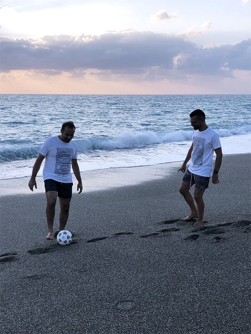 Due uomini indossano la T-shirt Bella sulla spiaggia al mare giocando a pallone.
