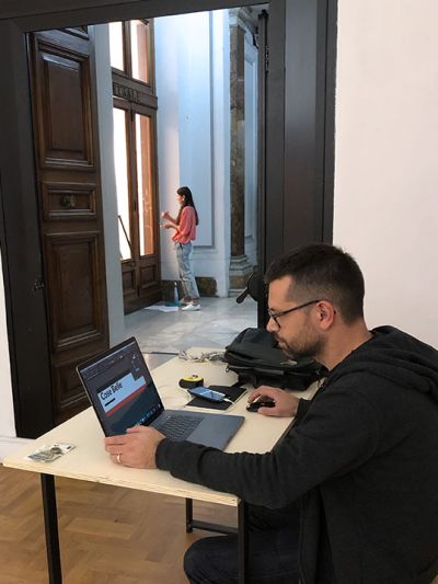 Alessandro Ledonne, designer of the team, works on his MacBook and Darina Birulina, illustrator of the team, paints the museum windows during the preparation phase of the Cose Belle Festival 2019.